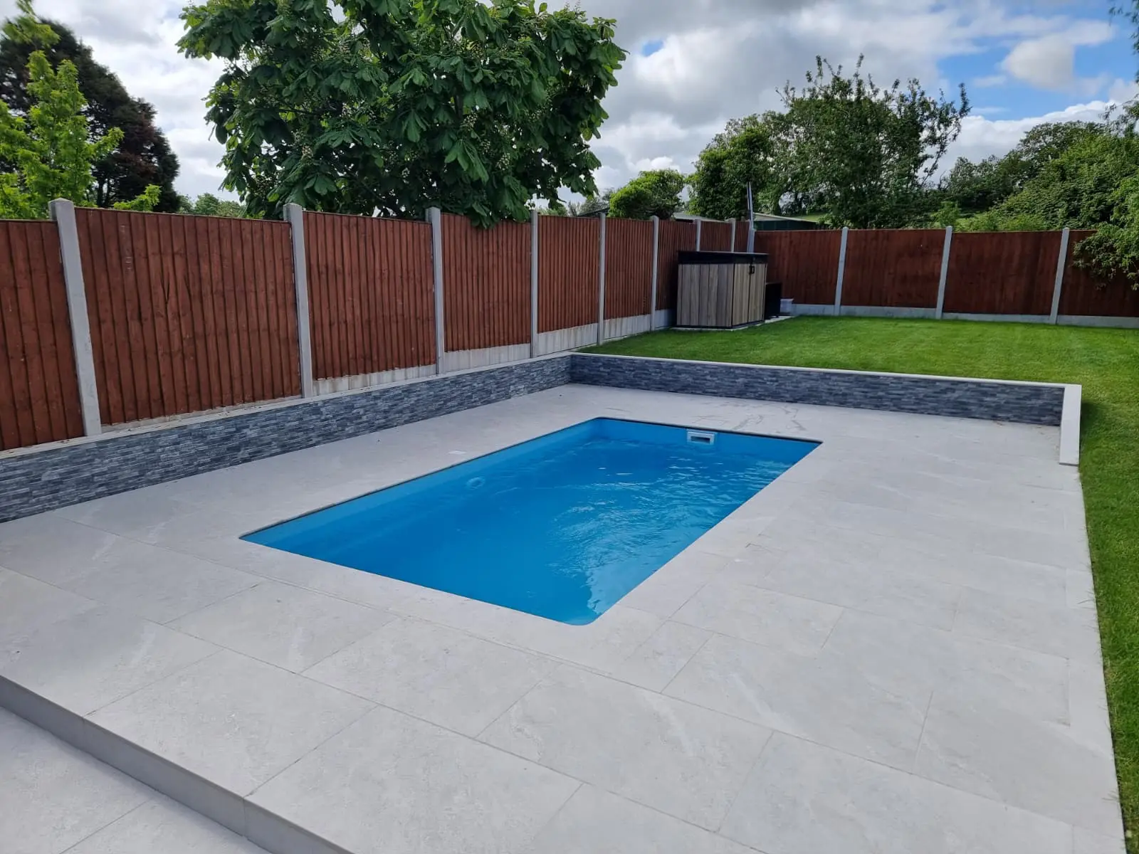Swimming pool surrounded by pale paving and landscaped garden